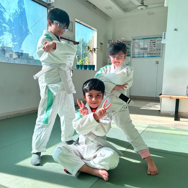 Kids in white gis playing on the mats in a sunlit room