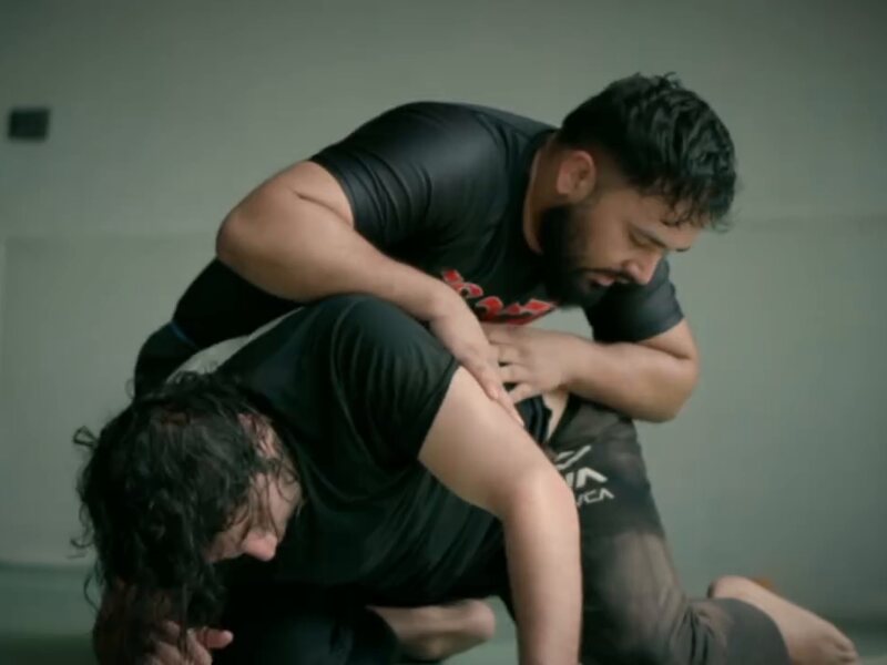A grappler in a rash guard controlling his partner from the top in No Gi class